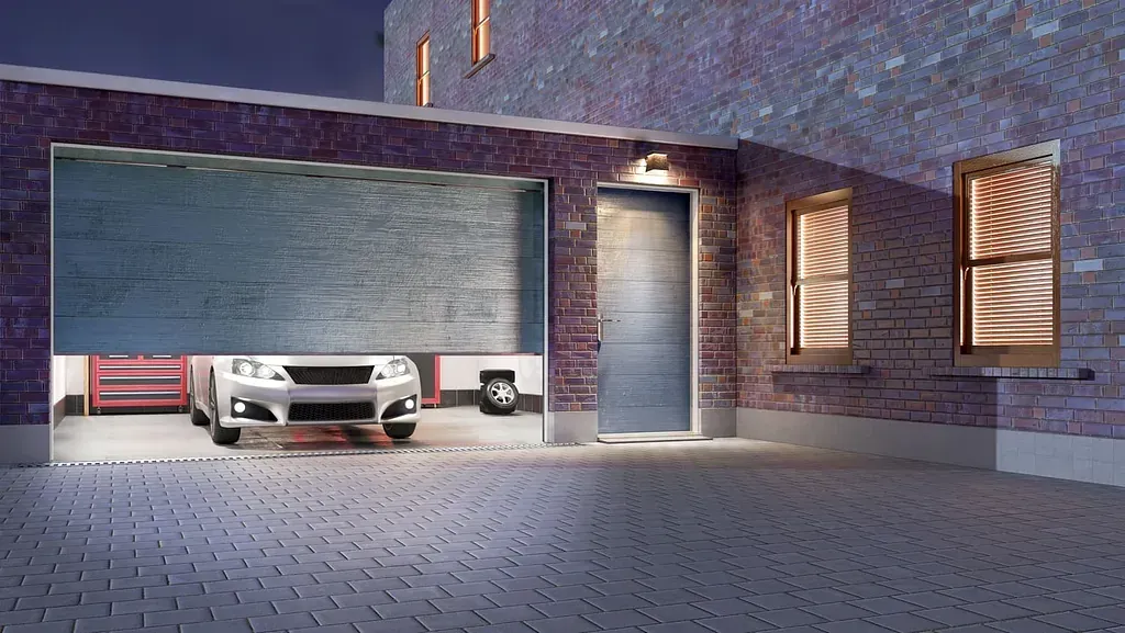 Coche en garaje abierto con puerta y ventanas en edificio de ladrillo por la noche.