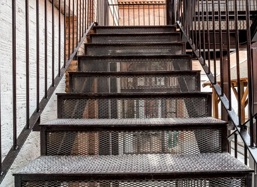 Escalera de incendios de metal, oscura, con peldaños de malla de diamante, que conduce hacia arriba.
