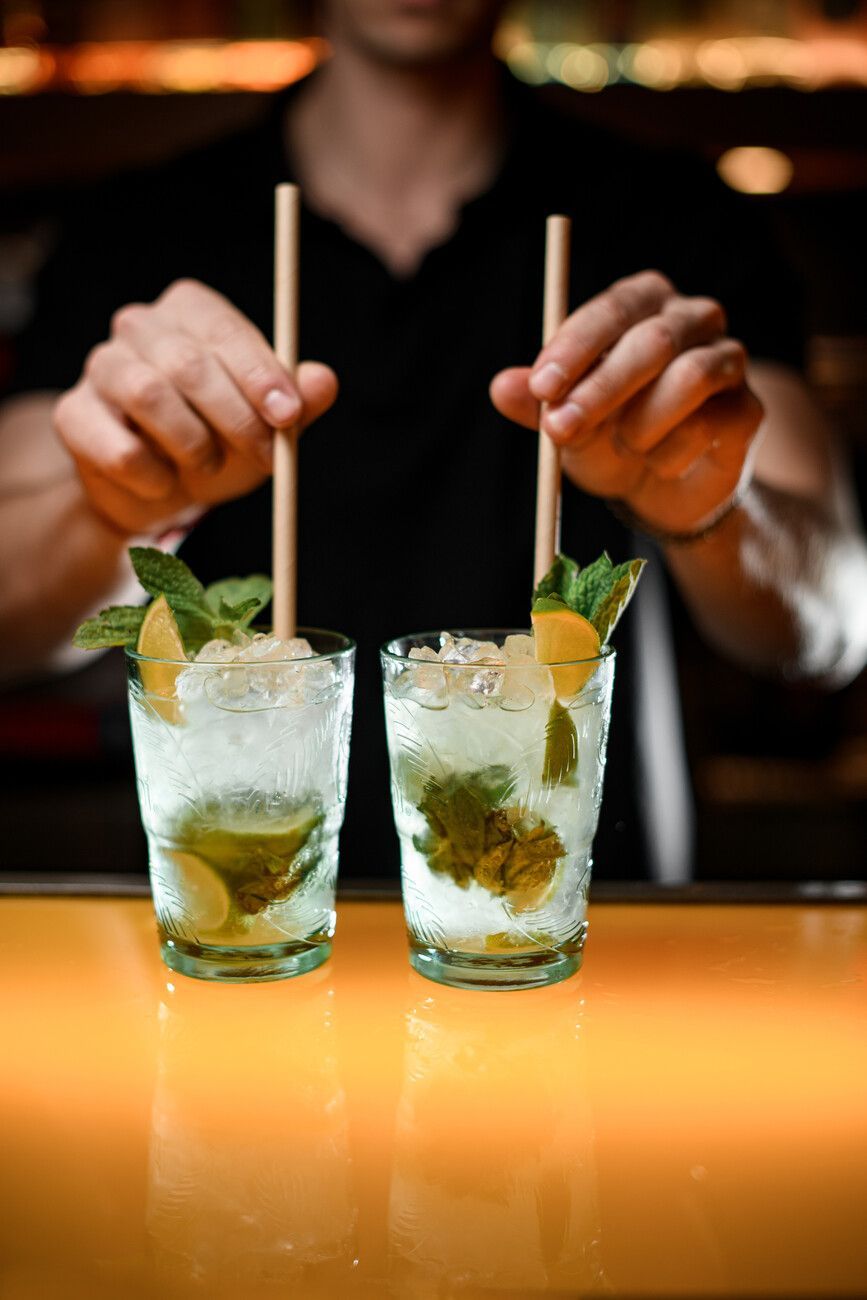 Un camarero sostiene dos vasos de mojito con pajitas.