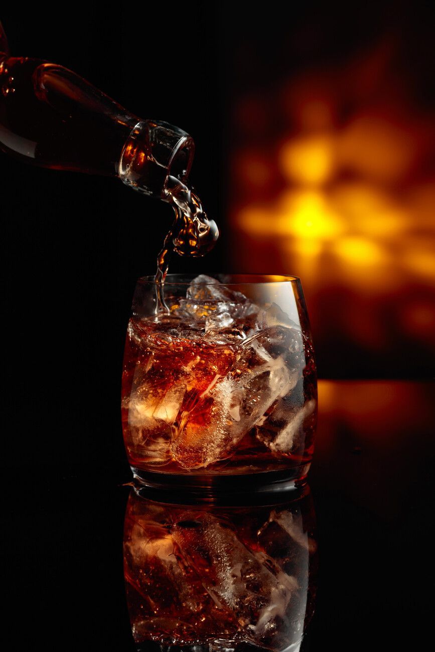 Una persona está vertiendo whisky en un vaso con cubitos de hielo.