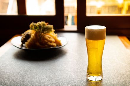 Un vaso de cerveza está sobre una mesa al lado de un plato de comida.