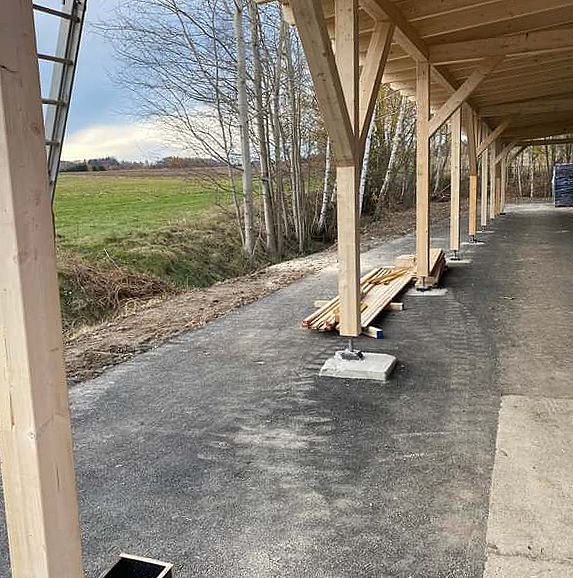 Ein überdachter Gehweg mit Holzbalken und einem Feld im Hintergrund.