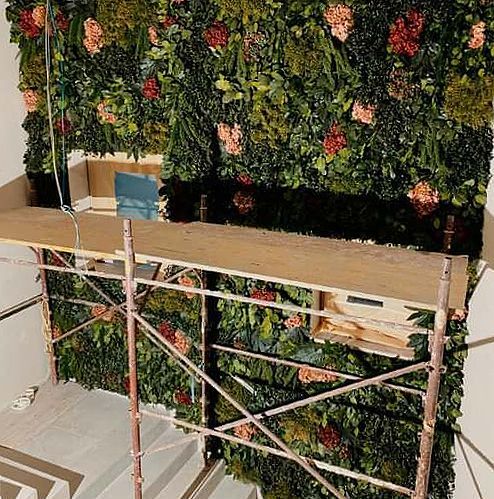 Auf einem Gerüst wird eine grüne Wand mit Blumen und Blättern aufgebaut.