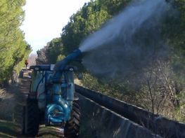 Un tractor azul está rociando agua sobre una valla.