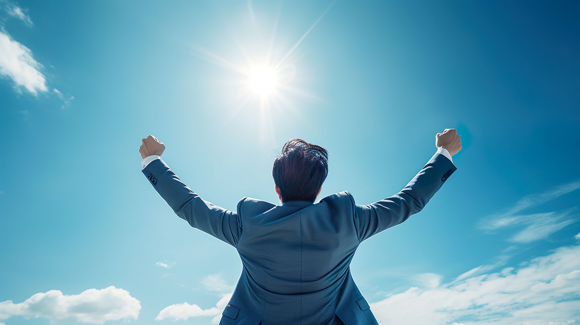 Un homme en costume, les bras levés vers un soleil éclatant dans un ciel bleu.