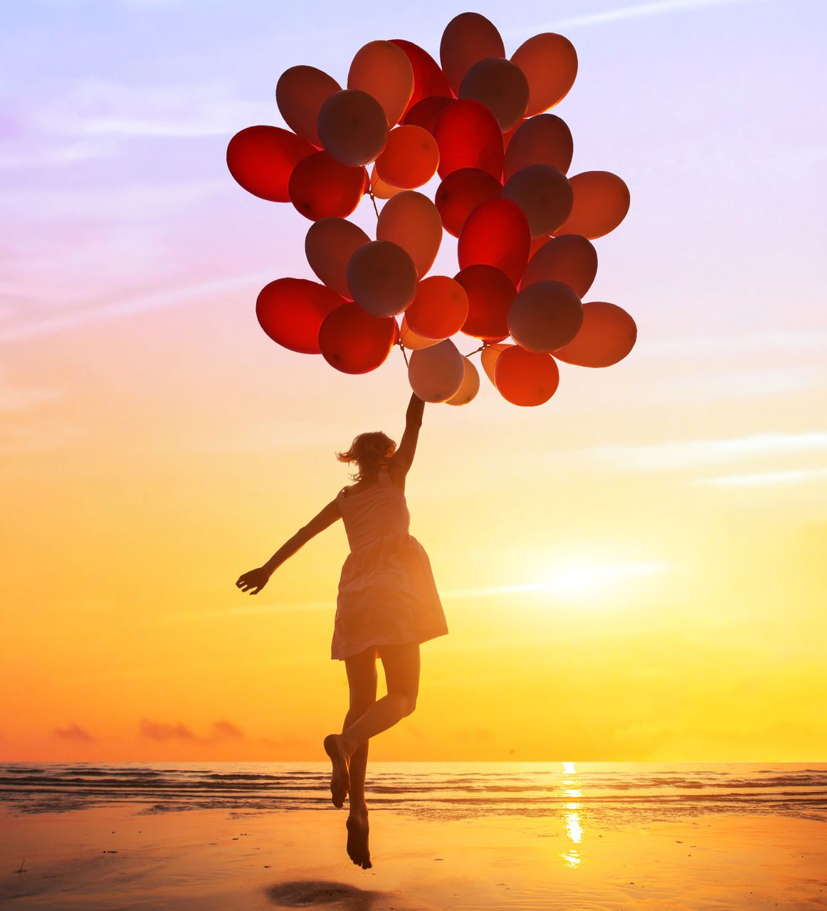 Silhouette d'une personne flottant avec des ballons sur fond de coucher de soleil sur l'océan.