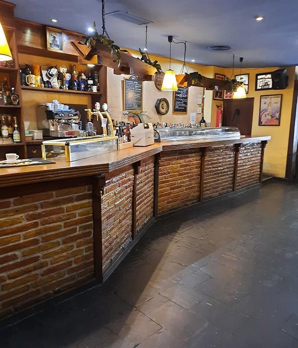 Acogedor café-bar con mostradores de ladrillo, lámparas colgantes, estantes con botellas y suelo de baldosas.