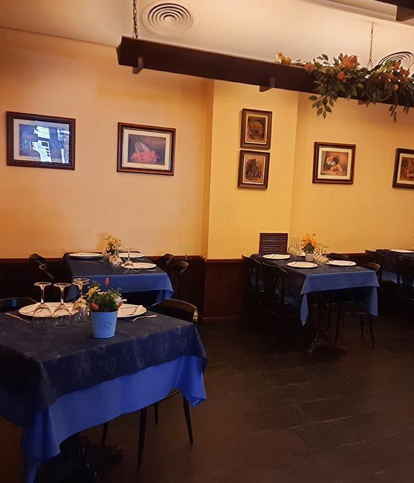 Acogedor comedor de restaurante con manteles azules, cuadros enmarcados en las paredes y una cálida iluminación amarilla.