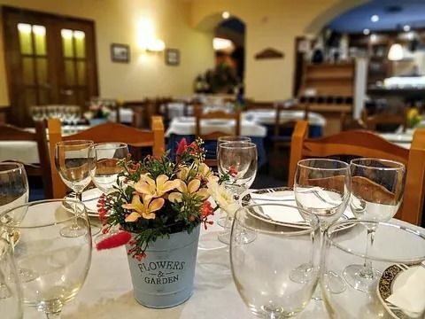 Mesa de restaurante puesta con copas de vino y platos, con un centro de mesa floral en una maceta azul.