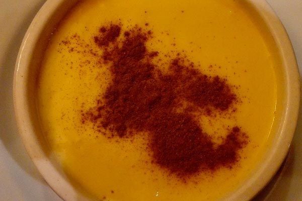 Tazón de sopa dorada coronado con una guarnición de especias de color rojo oscuro.
