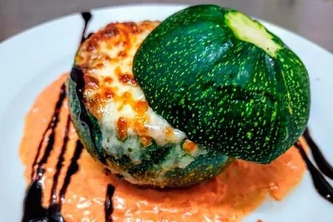 Calabacines rellenos de queso fundido en un plato blanco, rociados con salsa de naranja y glaseado balsámico.