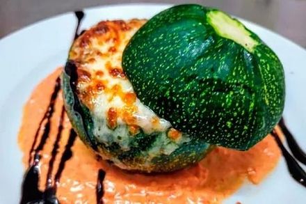Calabacines rellenos de queso fundido en un plato blanco, rociados con salsa de naranja y glaseado balsámico.