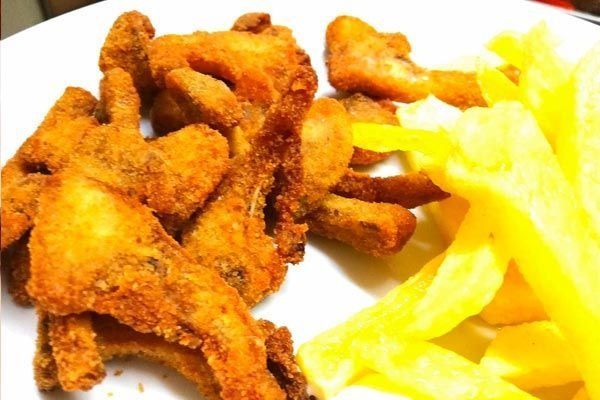 Tiras de pollo frito con papas fritas en un plato blanco.
