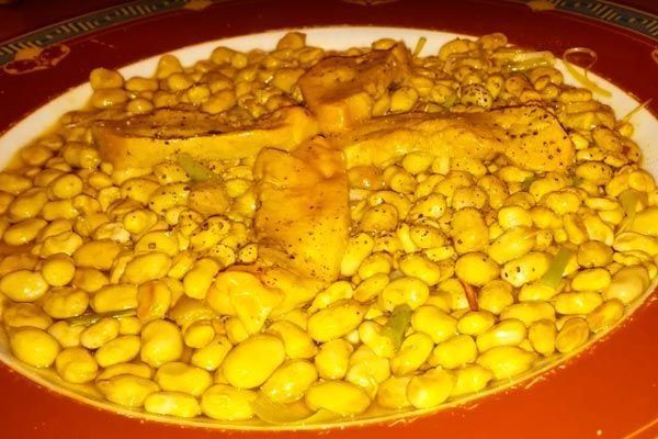 Plato de judías amarillas en un plato rojo, cubierto con trozos de pan o bollería.
