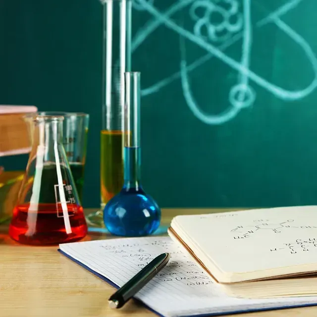 Un cuaderno y un bolígrafo sobre una mesa con una pizarra al fondo.