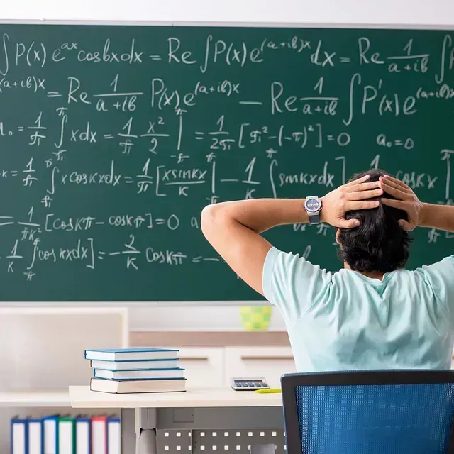 Un hombre está sentado frente a una pizarra con ecuaciones.