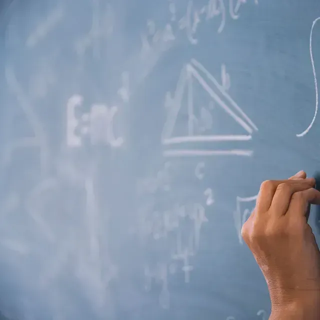 Una persona está escribiendo en una pizarra con tiza.