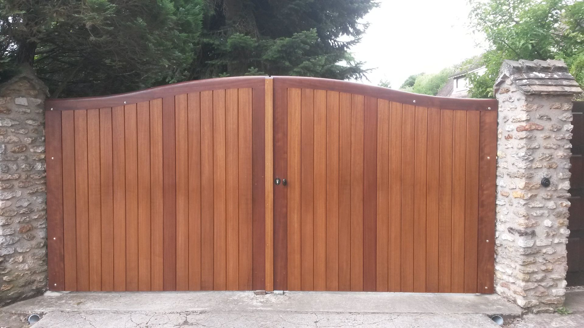 Deux portails d'allée en bois arqués, à lattes verticales, placés entre deux piliers en pierre.