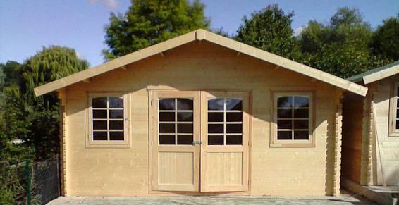 Une cabane en bois clair avec un toit à pignon, des portes doubles et deux fenêtres de chaque côté, située à l'extérieur.