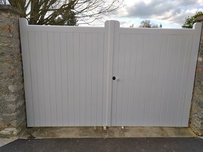 Un large portail en bois blanc à double vantail, avec des lattes verticales, situé entre deux piliers de pierre.