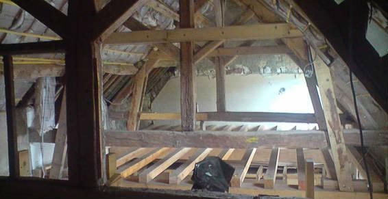 Un grenier inachevé avec des chevrons en bois apparents, des poutres de charpente et une structure de plancher en solives en construction.