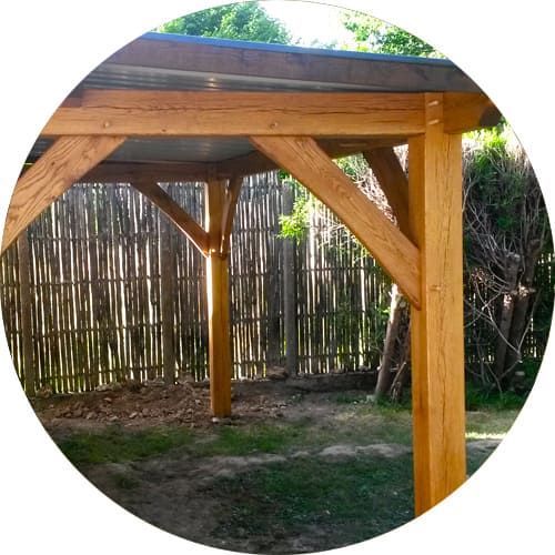 Pergola en bois avec des équerres d'angle diagonales adossée à une clôture en roseaux dans un jardin.