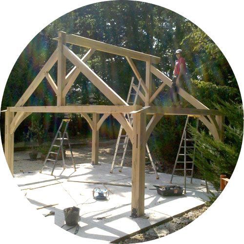 Une personne est assise sur la charpente en bois d'un bâtiment en construction, avec des échelles et des outils sur une base en béton.