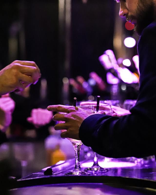 Un barman prépare des boissons sous un éclairage violet dans un bar.