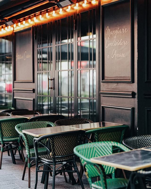 Restaurant en plein air avec façade noire, chaises et tables en osier vert.