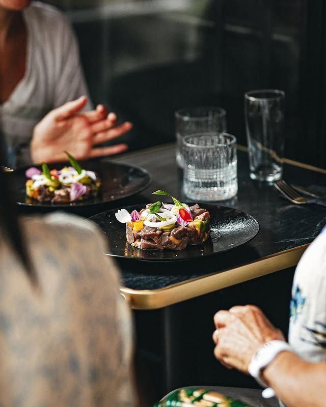 Deux assiettes de nourriture décorées de fleurs sont disposées sur une table entre des personnes assises, accompagnées de verres d'eau.
