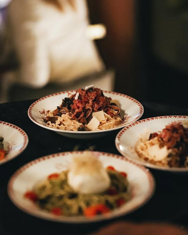Assiettes de pâtes garnies, servies sur un plateau noir, assiettes à bord rouge, personne floue en arrière-plan.