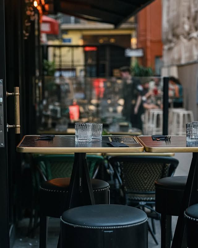 Terrasse extérieure ; tables et chaises. Une personne est visible à l’intérieur du restaurant.