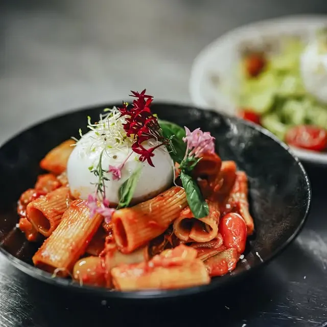 Plat de pâtes avec une grosse burrata, de la sauce tomate et une garniture.
