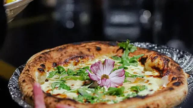Gros plan sur une pizza à la croûte dorée, au fromage blanc, aux herbes vertes et décorée d'une fleur rose.