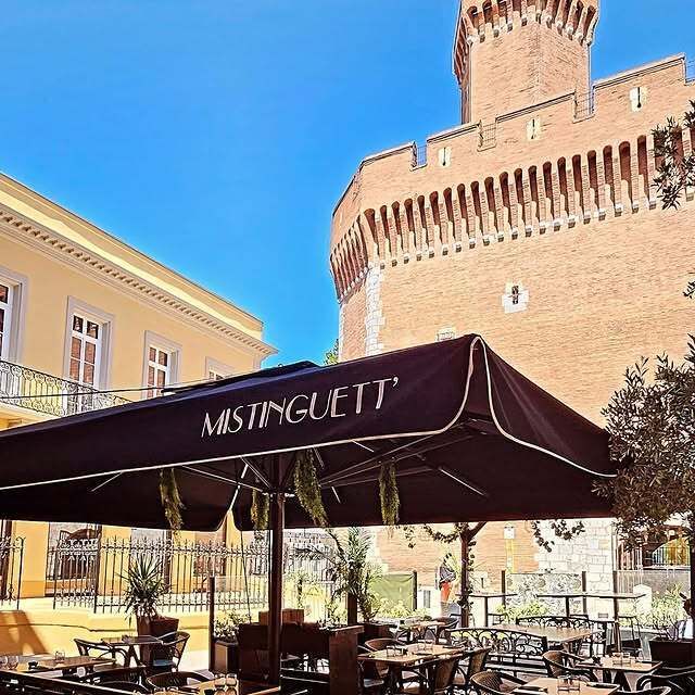 Restaurant avec terrasse, bâtiment en briques rouges en arrière-plan, journée ensoleillée.