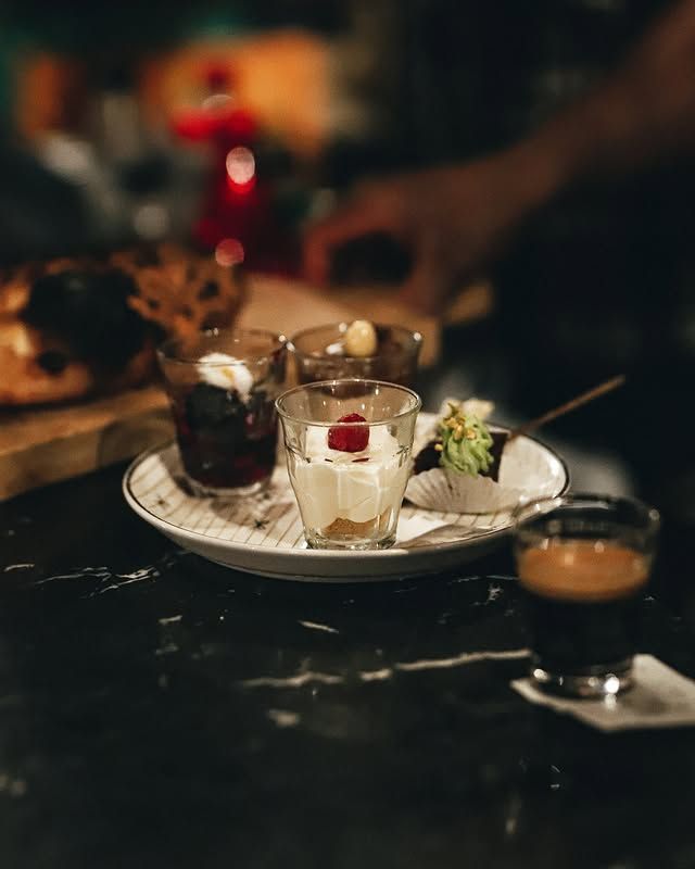 De petits desserts sur une assiette, à côté d'un café, sur un comptoir sombre.