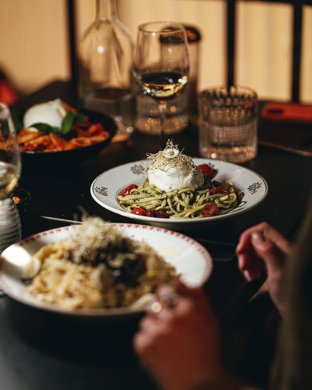 Des plats de pâtes, accompagnés de verres à vin, notamment de burrata et de pesto, dans une ambiance tamisée.