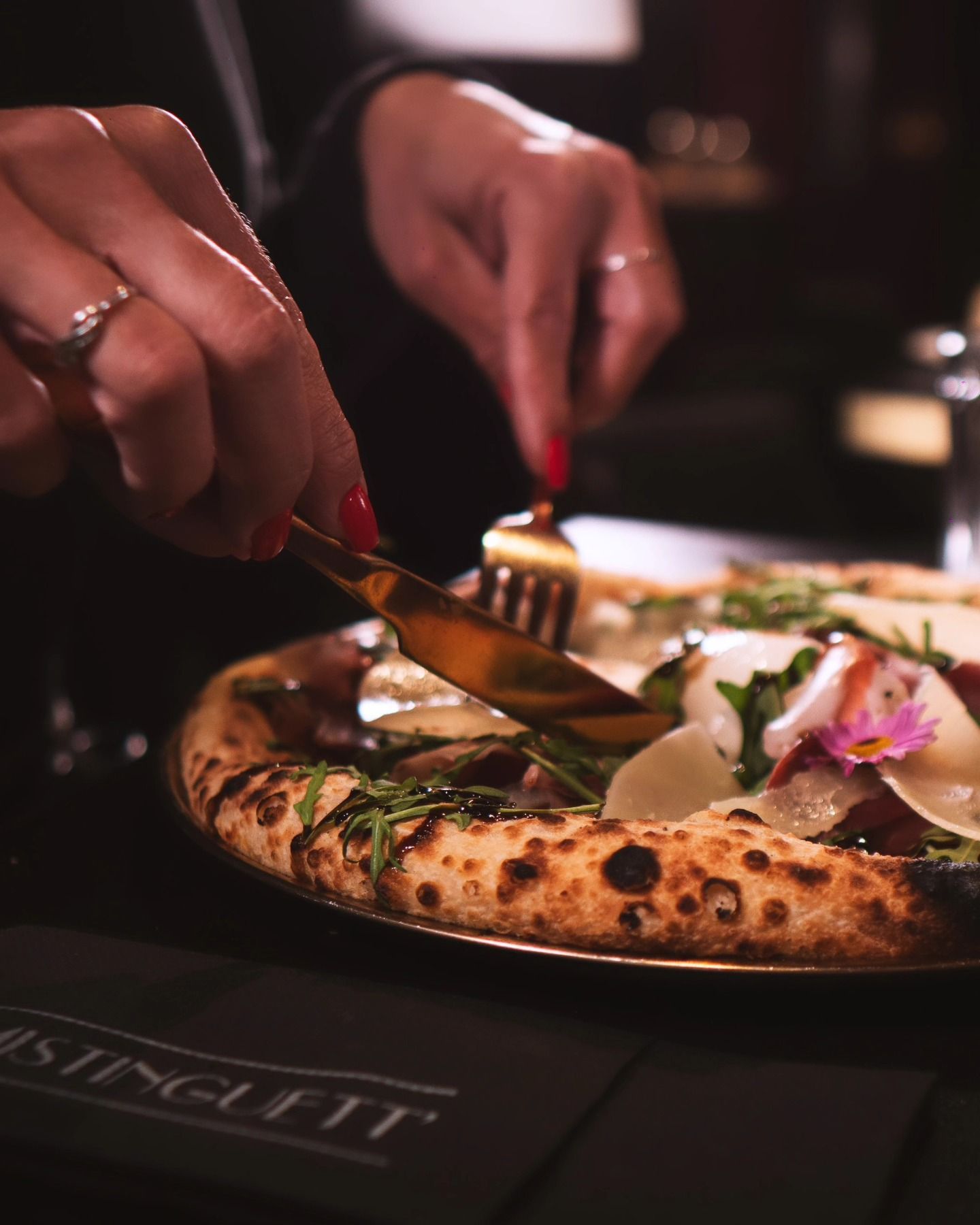 Une personne coupant une pizza gastronomique avec des ustensiles en or dans un restaurant.