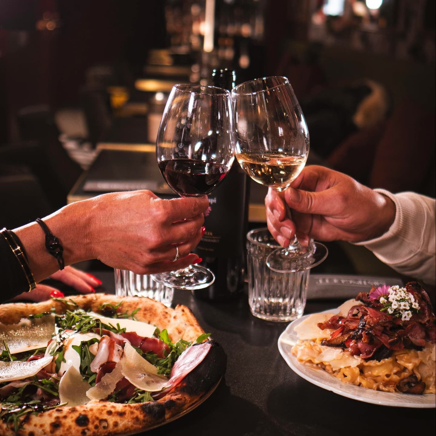 Des personnes trinquent avec des verres de vin en dégustant des pizzas et des pâtes à la table d'un restaurant.