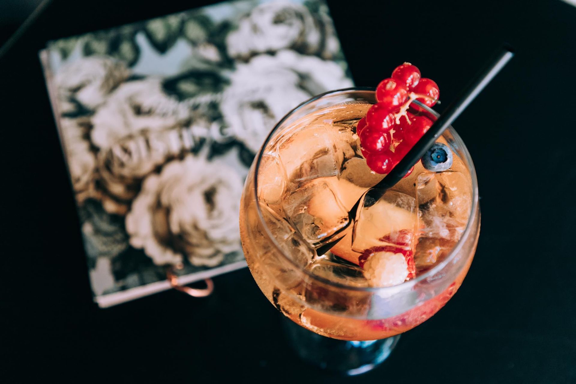 Un cocktail avec des glaçons, des baies et une paille, posé sur une table à côté d'un carnet à motifs floraux.