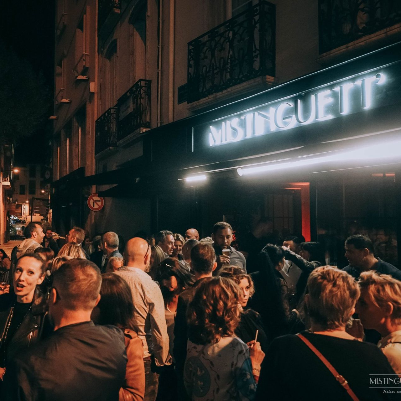 La nuit, une foule se presse devant l'entrée du restaurant, illuminée par une enseigne néon.