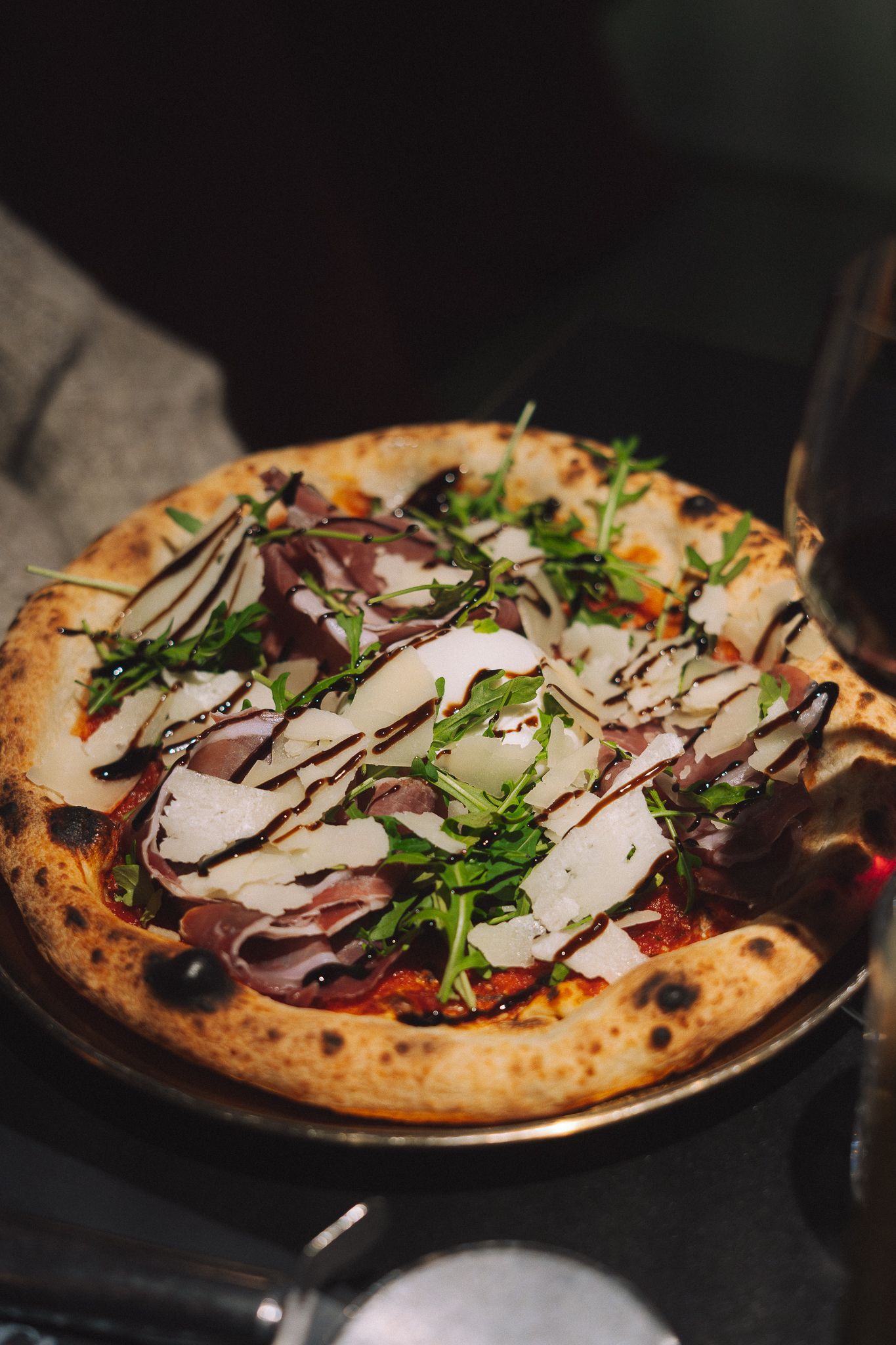 Pizza au prosciutto, à la roquette et au parmesan râpé, arrosée d'un filet de glaçage balsamique.