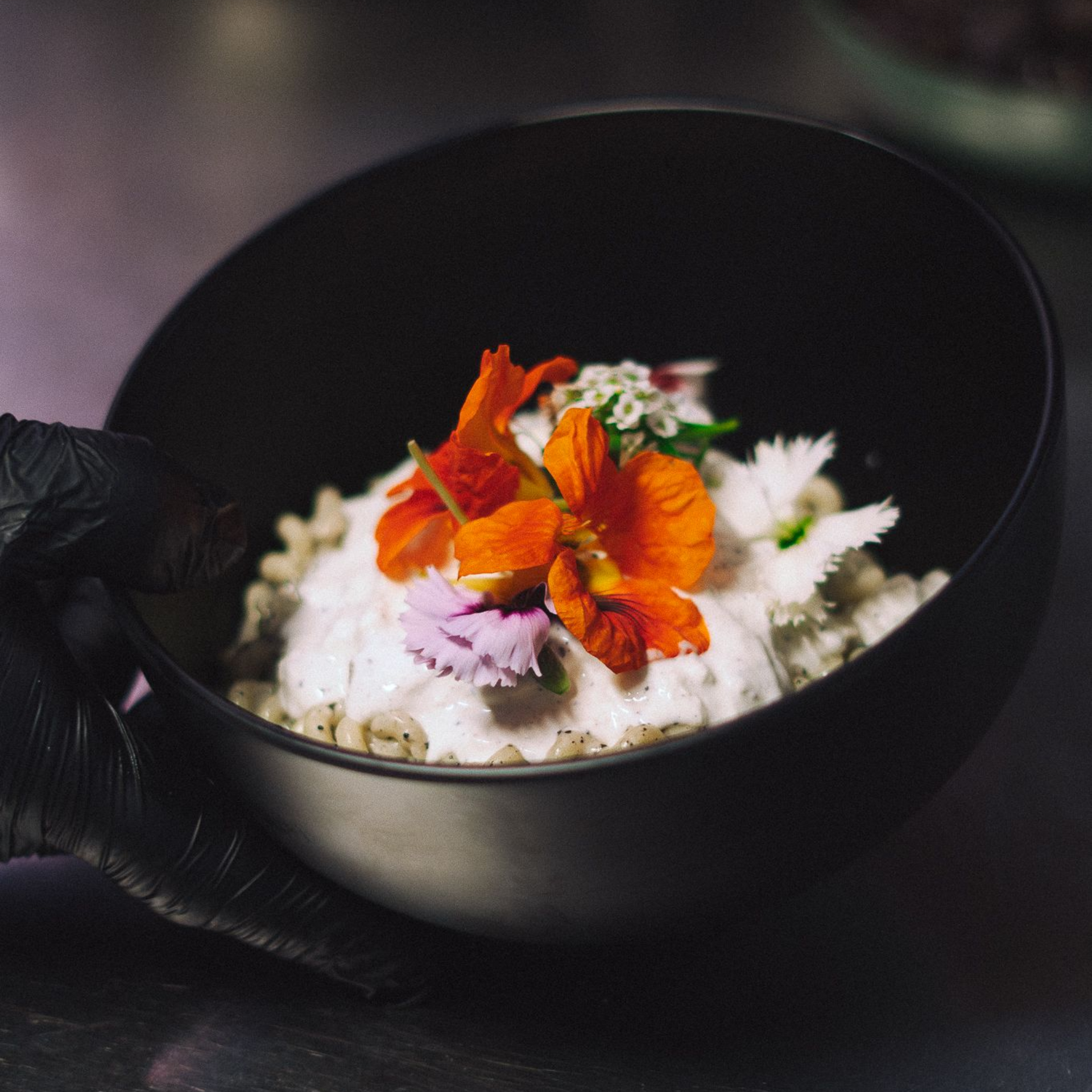 Bol noir contenant un plat crémeux, orné de fleurs orange et violettes.