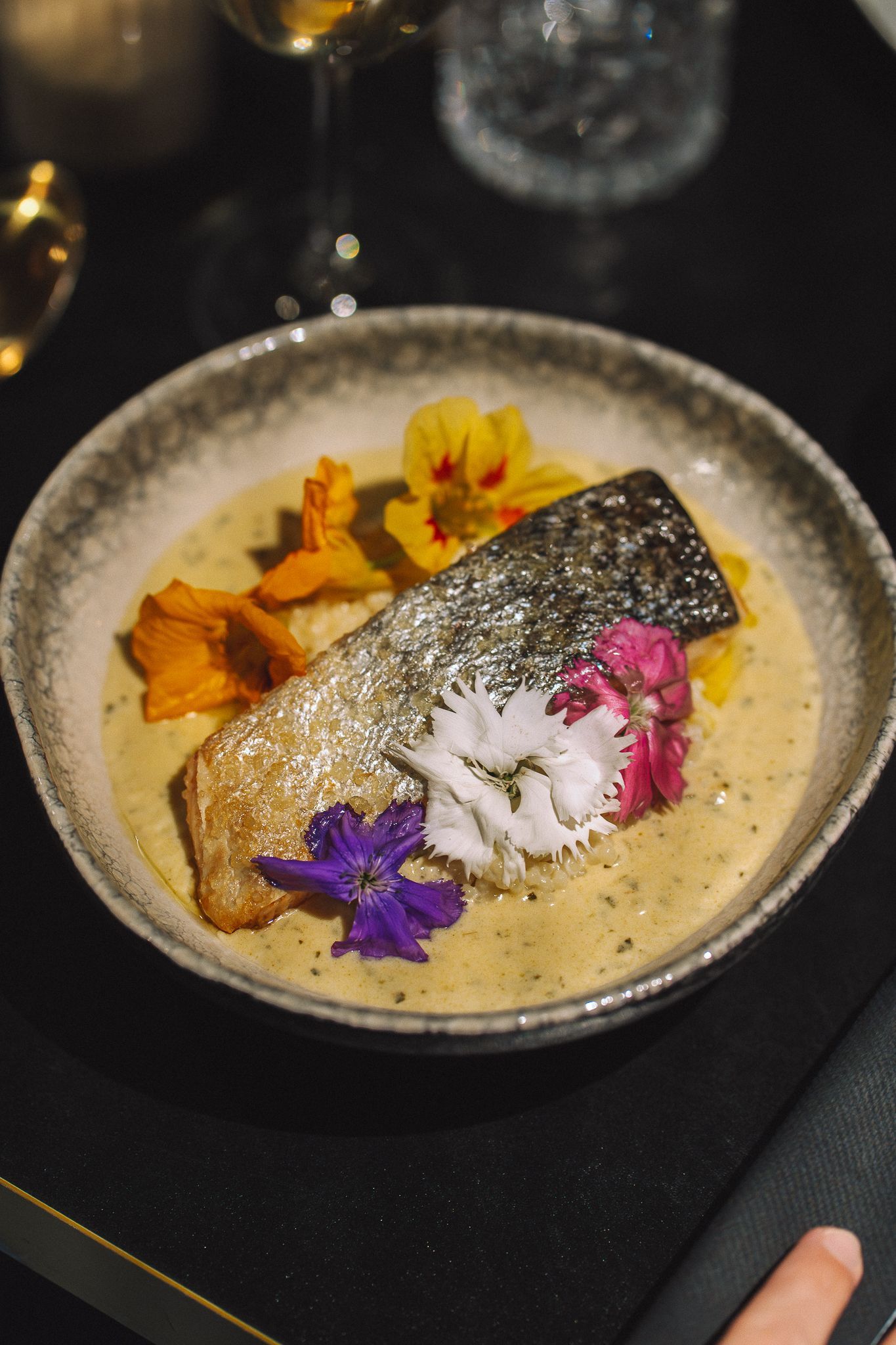 Saumon poêlé servi dans un bol avec sauce, fleurs comestibles et chips ; ambiance tamisée.