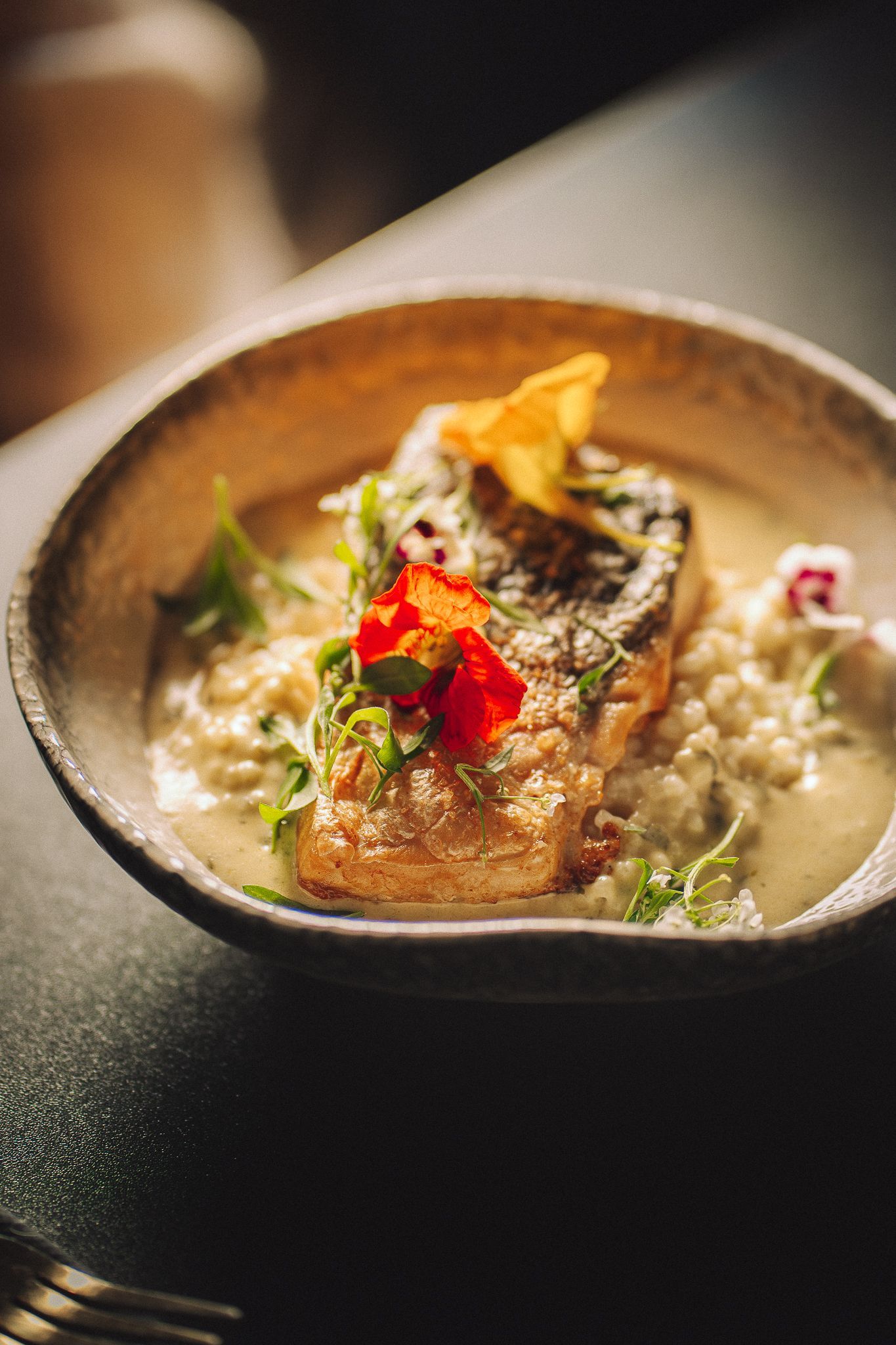 Poisson poêlé sur risotto, garni d'herbes et de pétales de fleurs dans un bol rustique.