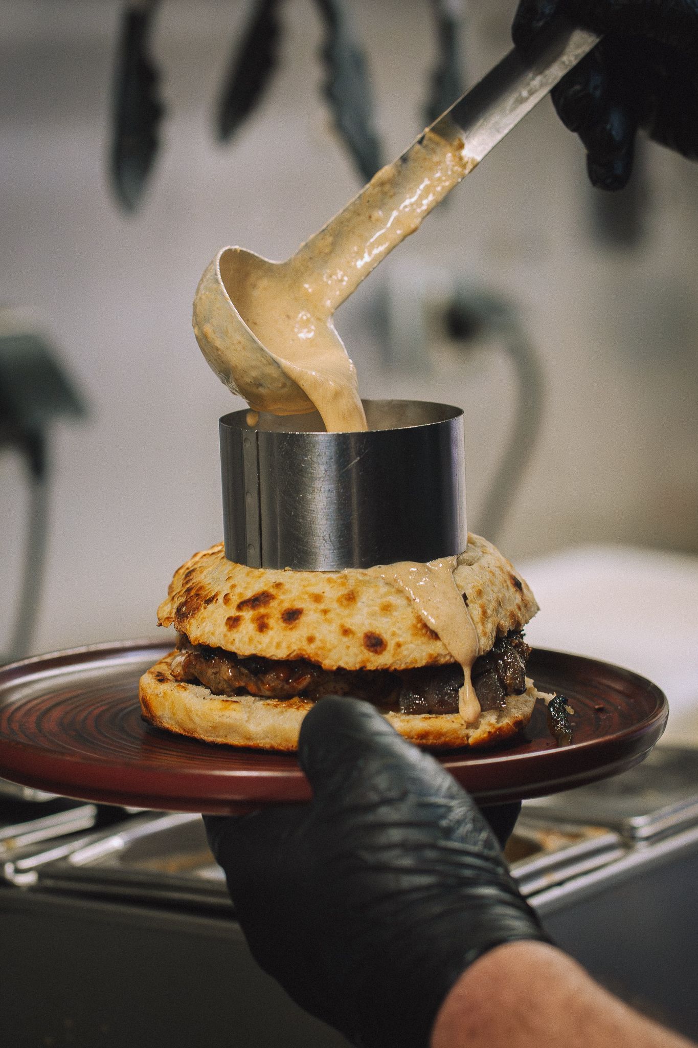 Un burger est présenté dans une assiette avec de la sauce versée à la louche à l'intérieur d'un anneau métallique.