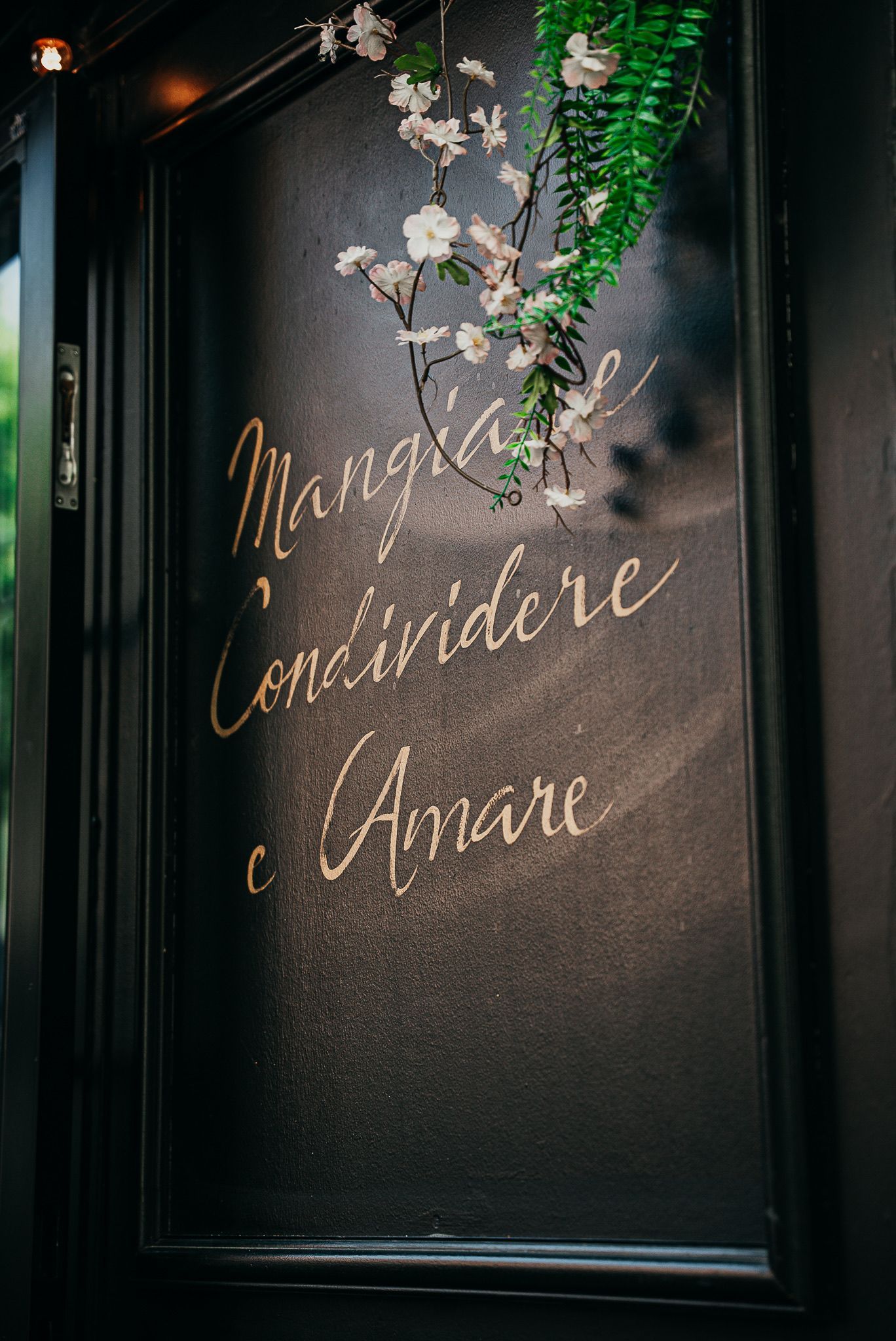 Porte noire avec inscription dorée, décorée de fleurs blanches et de feuilles vertes.