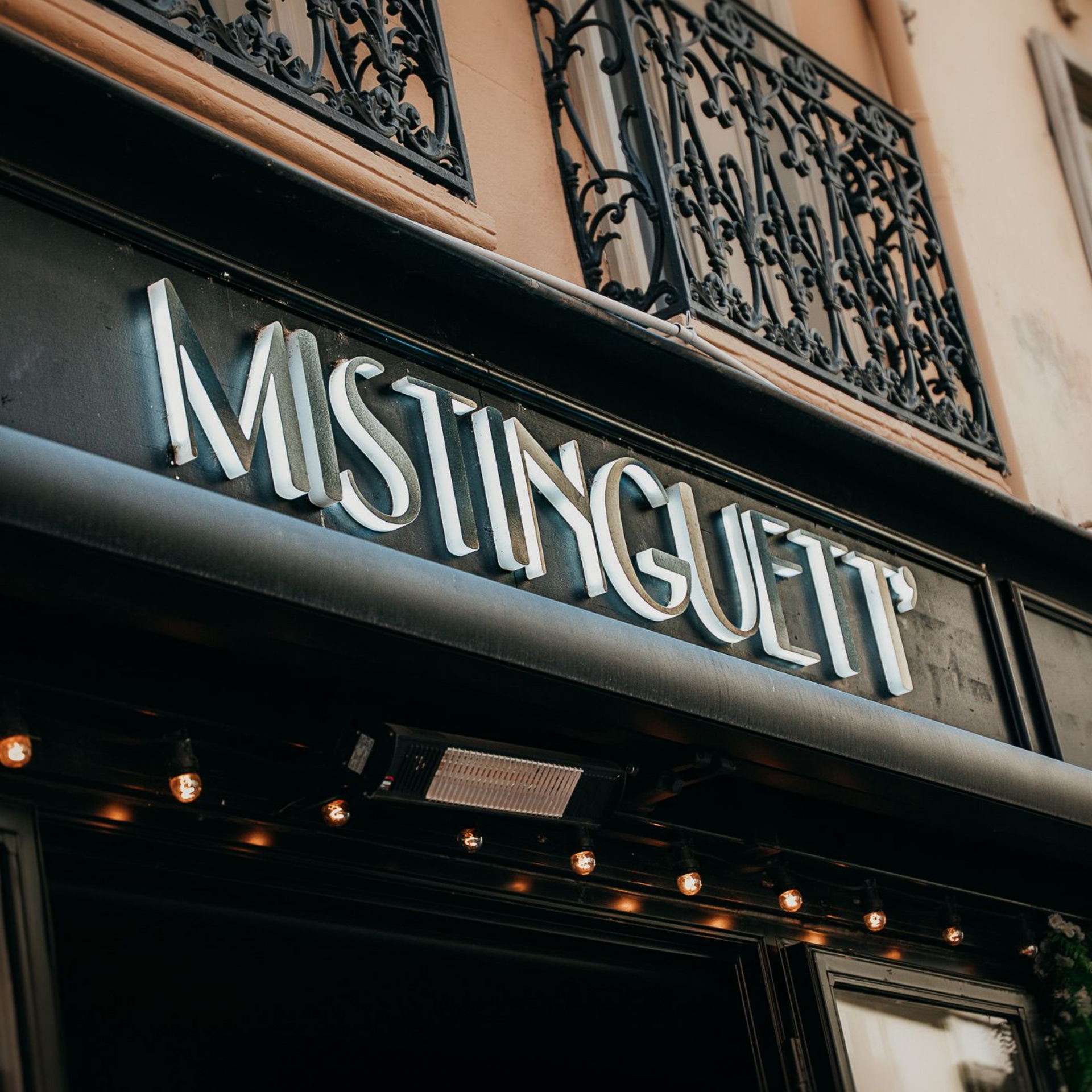 Enseigne du restaurant, en lettres blanches sur façade noire, éclairée par de petites lumières.
