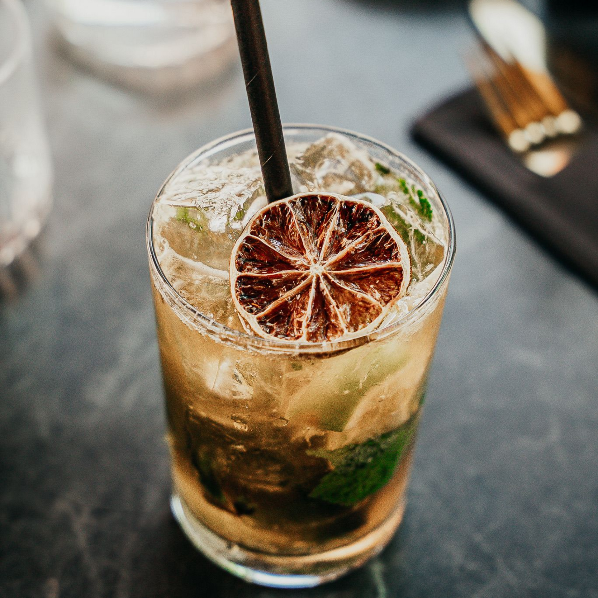 Cocktail servi dans un verre avec une rondelle de citron vert et une paille, sur un support sombre et texturé.