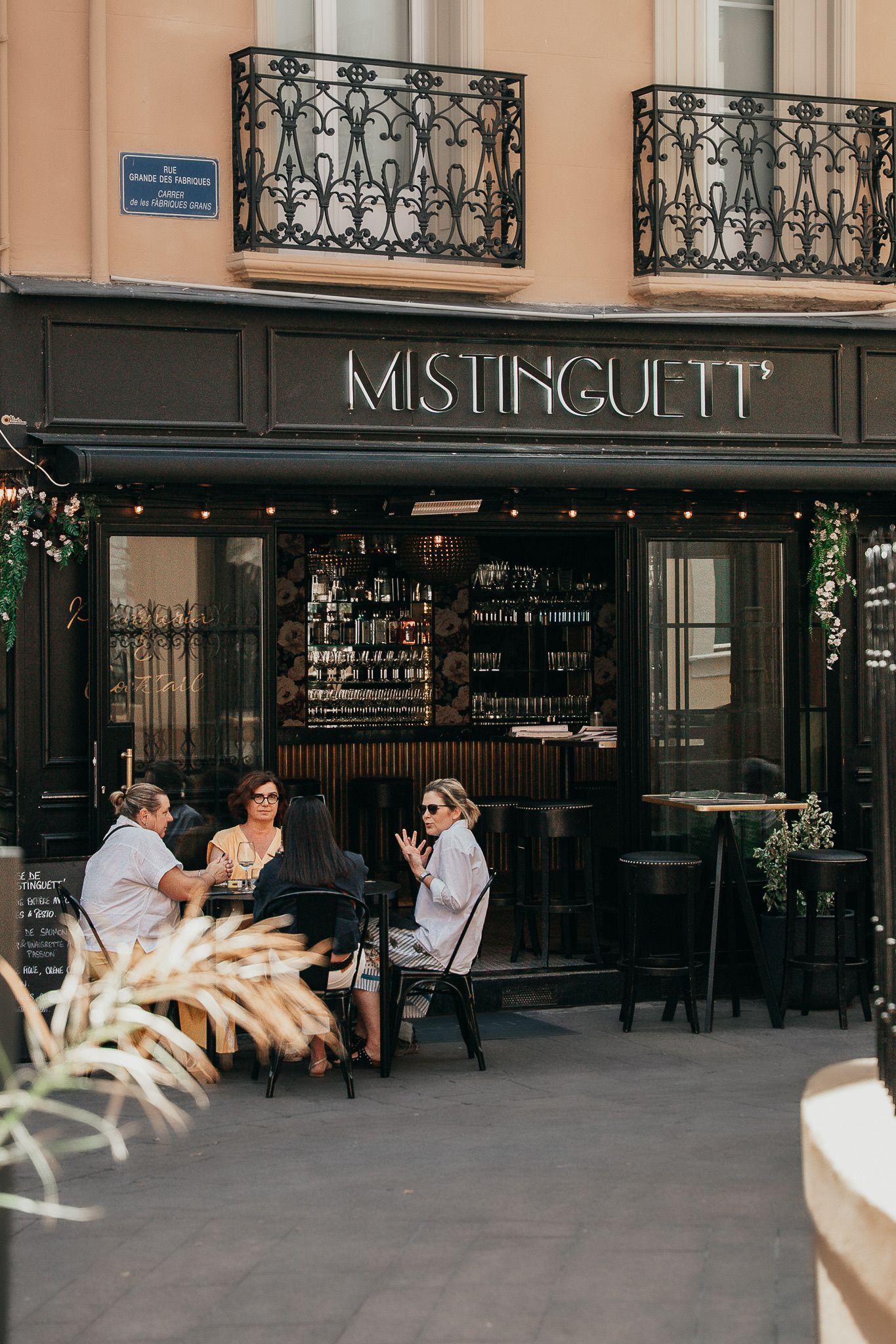 Des personnes attablées à la terrasse d'un restaurant, façade noire.